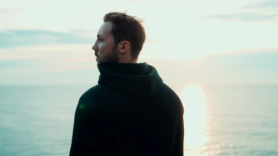 Pjotr Weiss im dunklen Hoodie am Meer bei tief stehender Sonne.